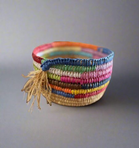 Colourful woven raffia basket with a tassel on a plain grey background