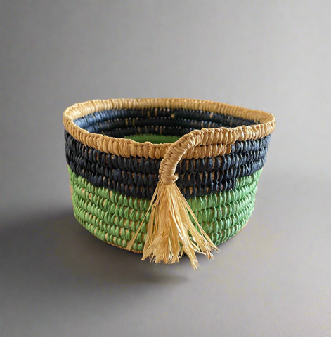 Woven basket with tassel made with green, blue and beige raffia on a gray background
