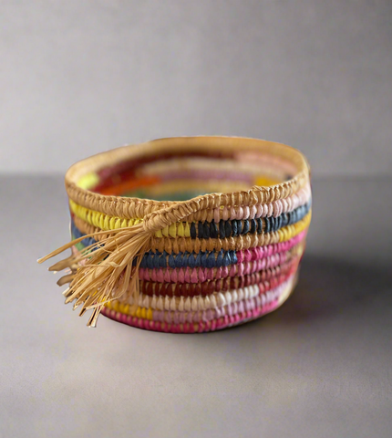 Colourful woven raffia basket with a tassel on a grey background