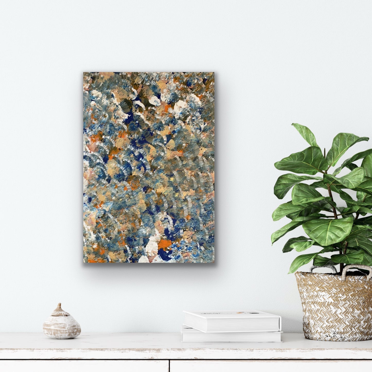 A painting by Belinda Golder Kngwarreye depicting bush plum dreaming hanging on a wall with a plant and decorative items below.