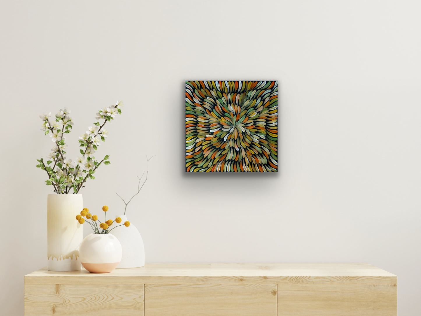 A painting by Mary Rumble featuring a pattern of intertwined leaves in various green, orange and white colours hanging on a wall above a modern wooden side table.