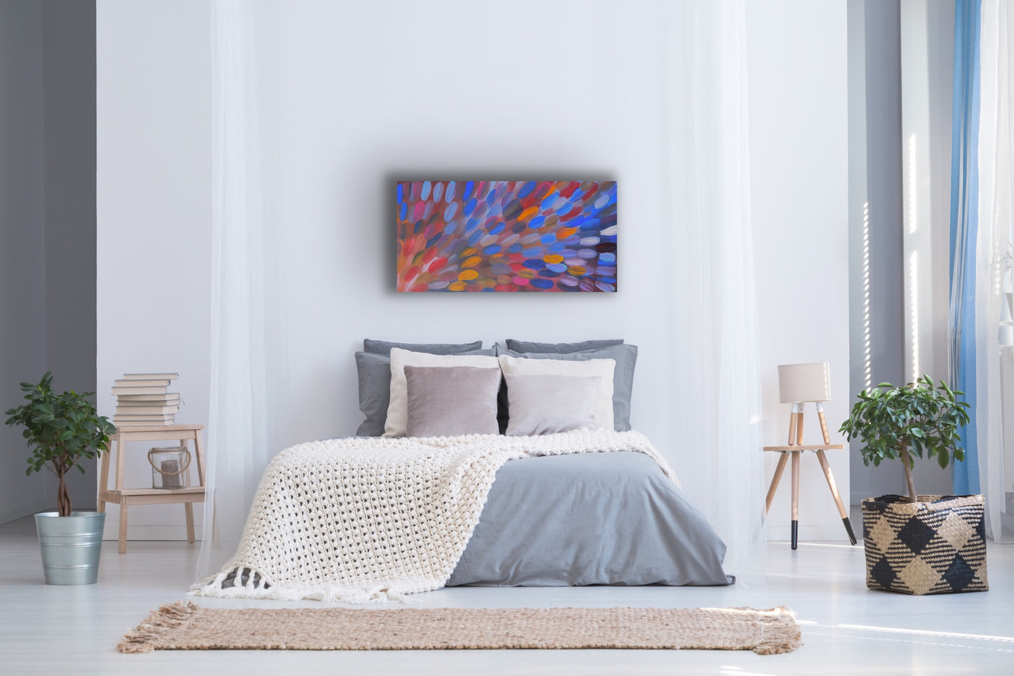 A 120x60cm painting by Gloria Petyarre hanging above a bed in a modern bedroom suite with a bed, abstract plants, side tables and a lamp.