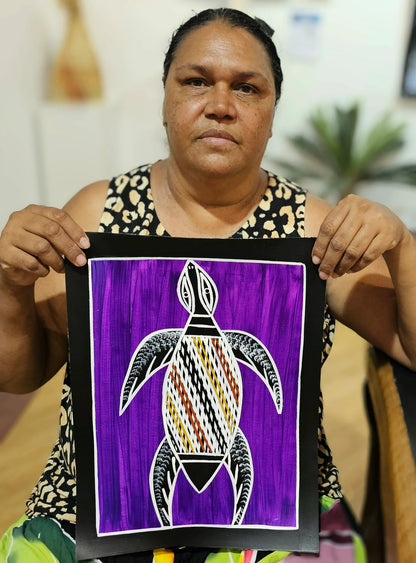 Artist Christine Burarrwanga holding her small painting depicting a sea turtle with traditional rarrk patterns on a purple background.