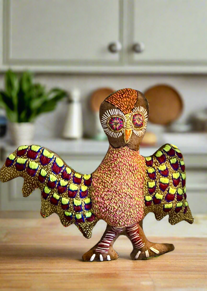 Decorative owl soft sculpture by Rhonda Sharpe with patterned, stitched feathers on a kitchen counter with cabinets and plants in the background