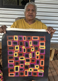Artist Abie Loy Kemarre holding her small Awelye painting with colourful geometric patterns and dotting.