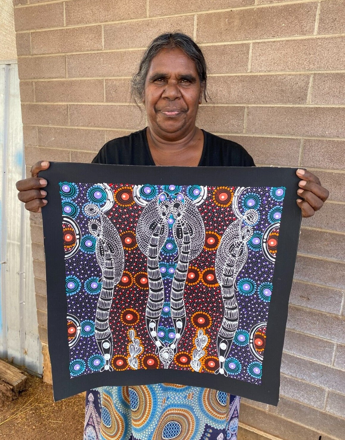 Colleen Wallace Nungarrayi holding her 45x45cm painting depicting her dreamtime sisters story.