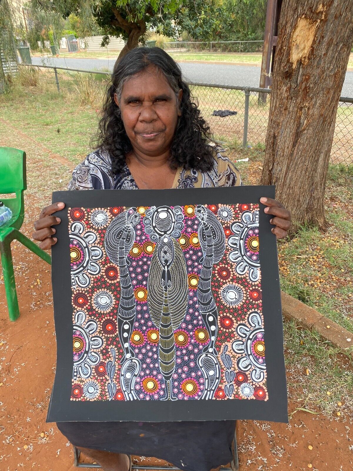 Colleen Wallace Nungarrayi holding her 45x45cm painting depicting her dreamtime sisters story.