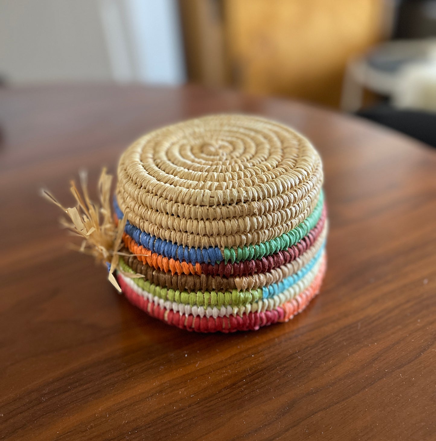 Colourful upside down woven raffia basket with a tassel on a wooden surface