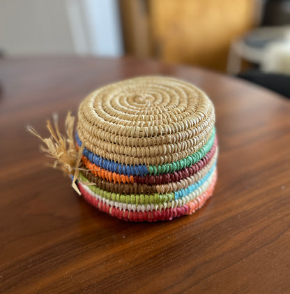 Colourful upside down woven raffia basket with a tassel on a wooden surface
