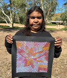 Bernadine Johnson Kemarre holding one of her 30x30cm paintings, representing traditional bush medicine plants.