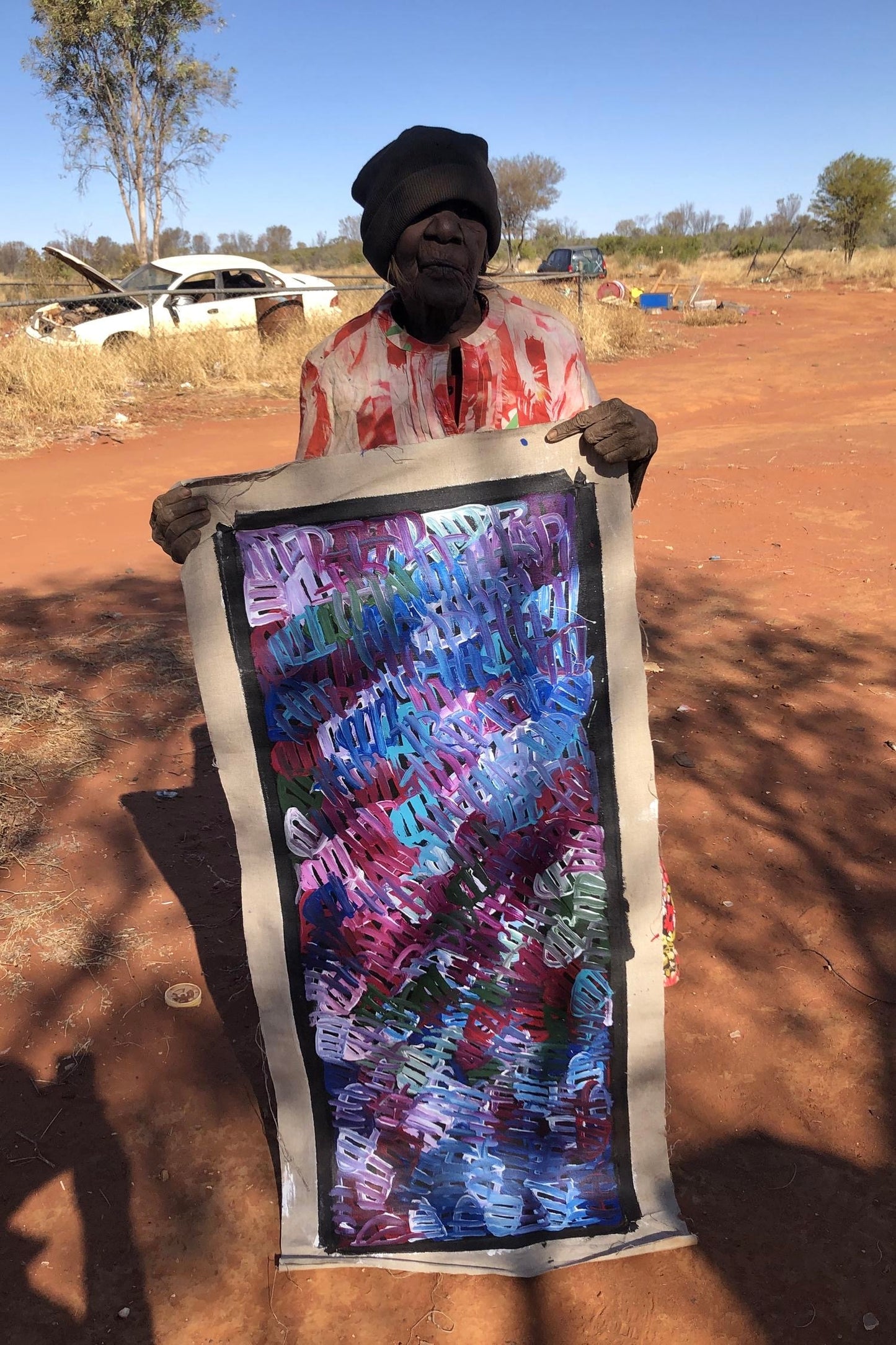 Emily Pwerle holding her painting representing awelye or women's ceremonies.