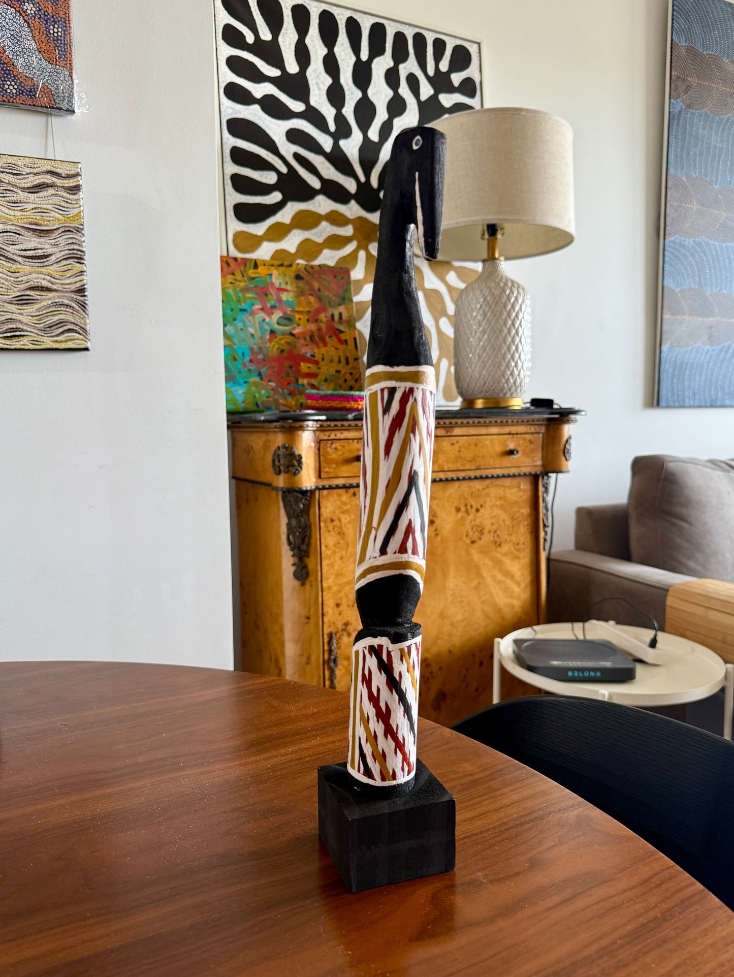 Painted milkwood bird carving by Aboriginal artist Christine Burarrwanga on a wooden table with a lamp and artwork in the background.