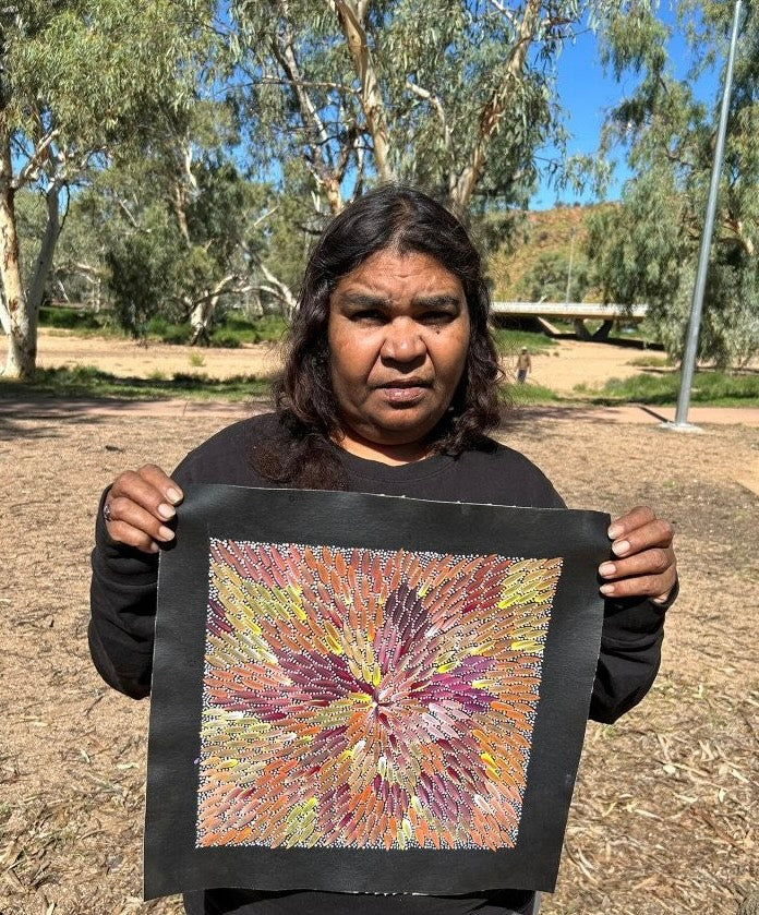 Bernadine Johnson Kemarre holding one of her 30x30cm paintings, representing traditional bush medicine plants.