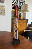 Painted milkwood bird carving by Aboriginal artist Christine Burarrwanga on a wooden table with a lamp and artwork in the background.