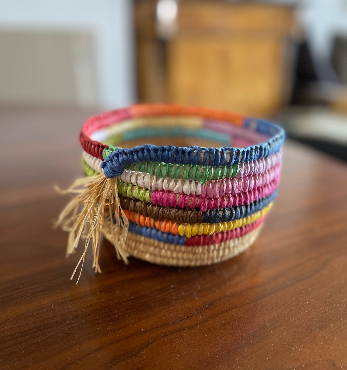 Colourful woven raffia basket with a tassel on a wooden surface.