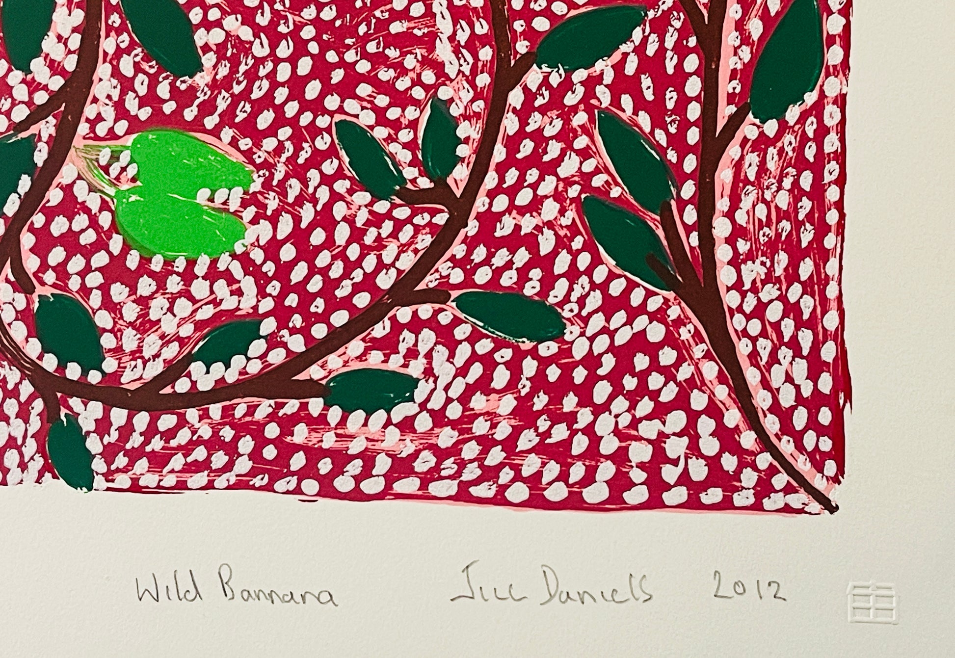 Close-up of a screen print by Jill Daniels 'Wild Banana', artwork depicts leaves and branches on a red and white patterned background