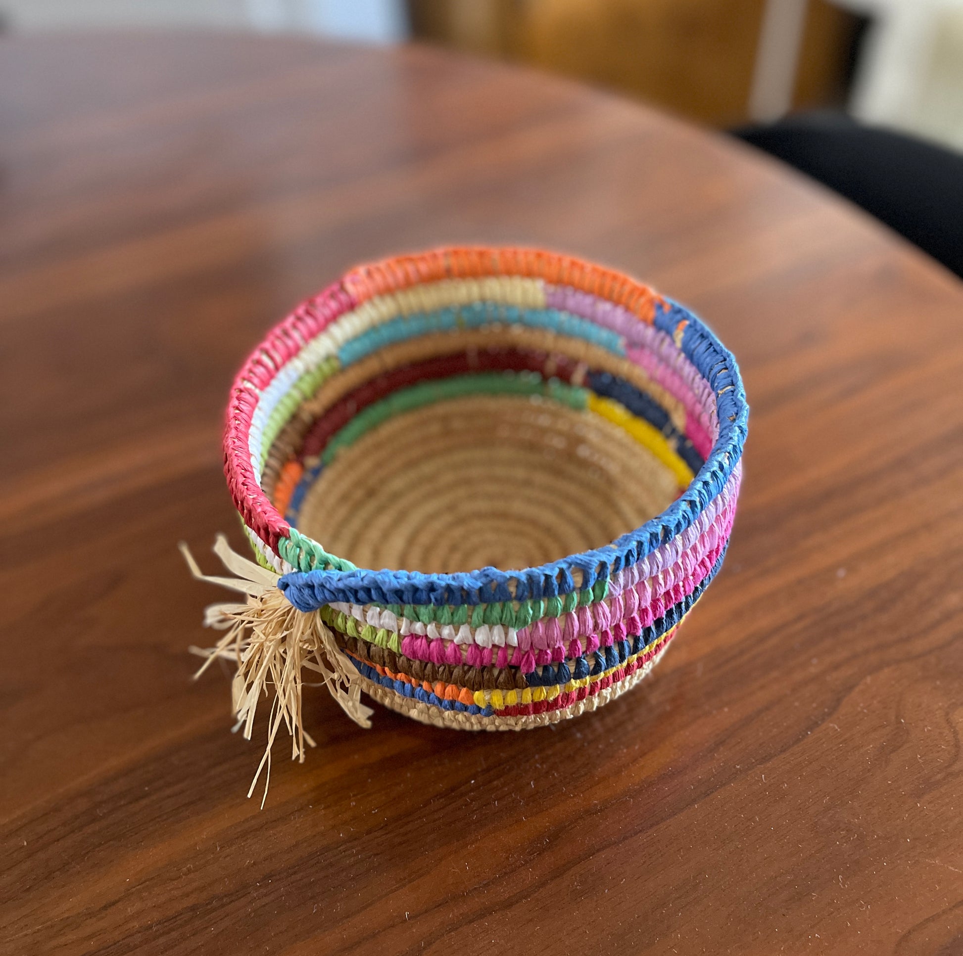 Colourful woven raffia basket with a tassel on a wooden surface