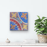 A painting by Anna Tilmouth on a white wall above a shelf with decor items and a plant.