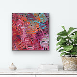 A painting by Emily Pwerle on a white wall above a shelf with decor items and a plant.