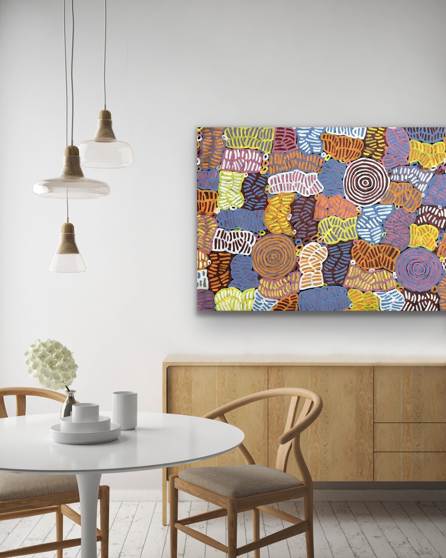 An awelye painting by Betty Club Mbitjana hanging on a white wall above a wooden console and dining setting.
