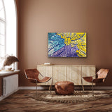 A painting by Lorna Fencer Napurrula depicting yarla or bush potato dreaming hanging in a modern living room with abstract art on the wall, brown chairs, and a wooden sideboard.