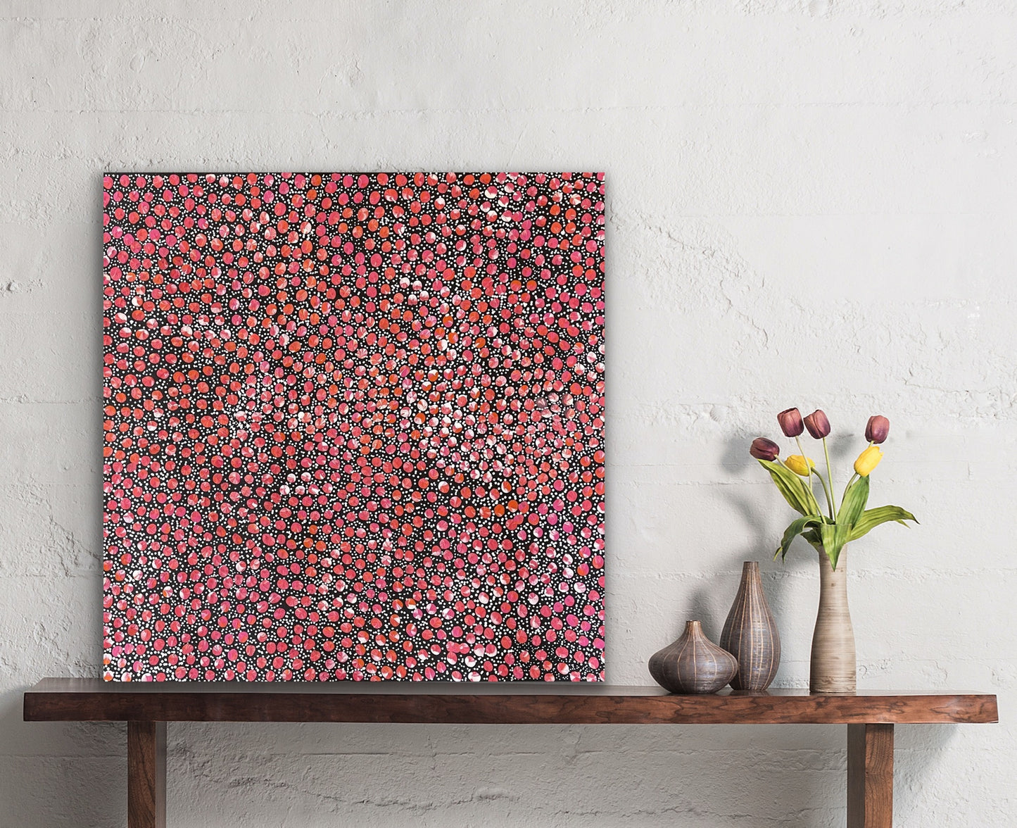 A painting by Eileen Bird Kngwarreye on a white wall, with a wooden console table and decorative items below.