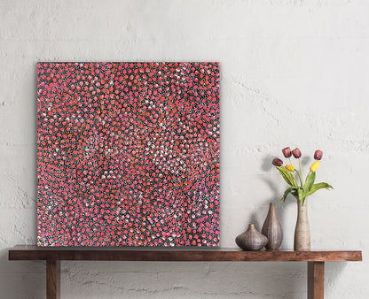 A painting by Eileen Bird Kngwarreye on a white wall, with a wooden console table and decorative items below.