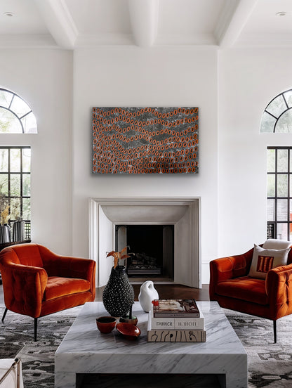 A painting by Ngoia Pollard Napalptjarri hanging in a modern living room with burnt orange chairs, a marble coffee table.