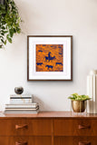 Framed artwork by Jill Daniels on a wall above a wooden console table with decorative items.