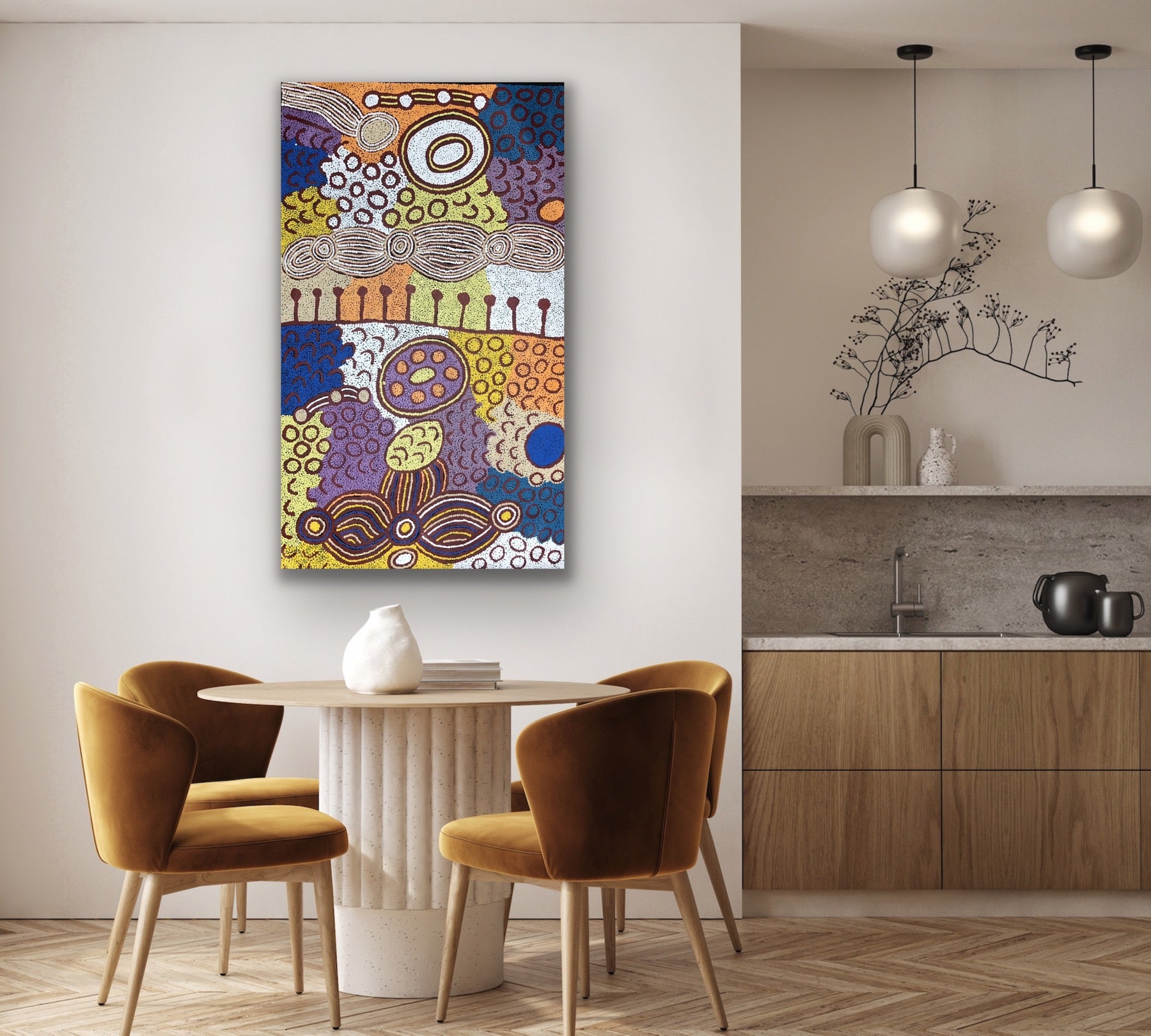 Dining area with an amazing colourful painting by Marlene Young Nungarrayi on the wall, wooden chairs, and a kitchen in the background.