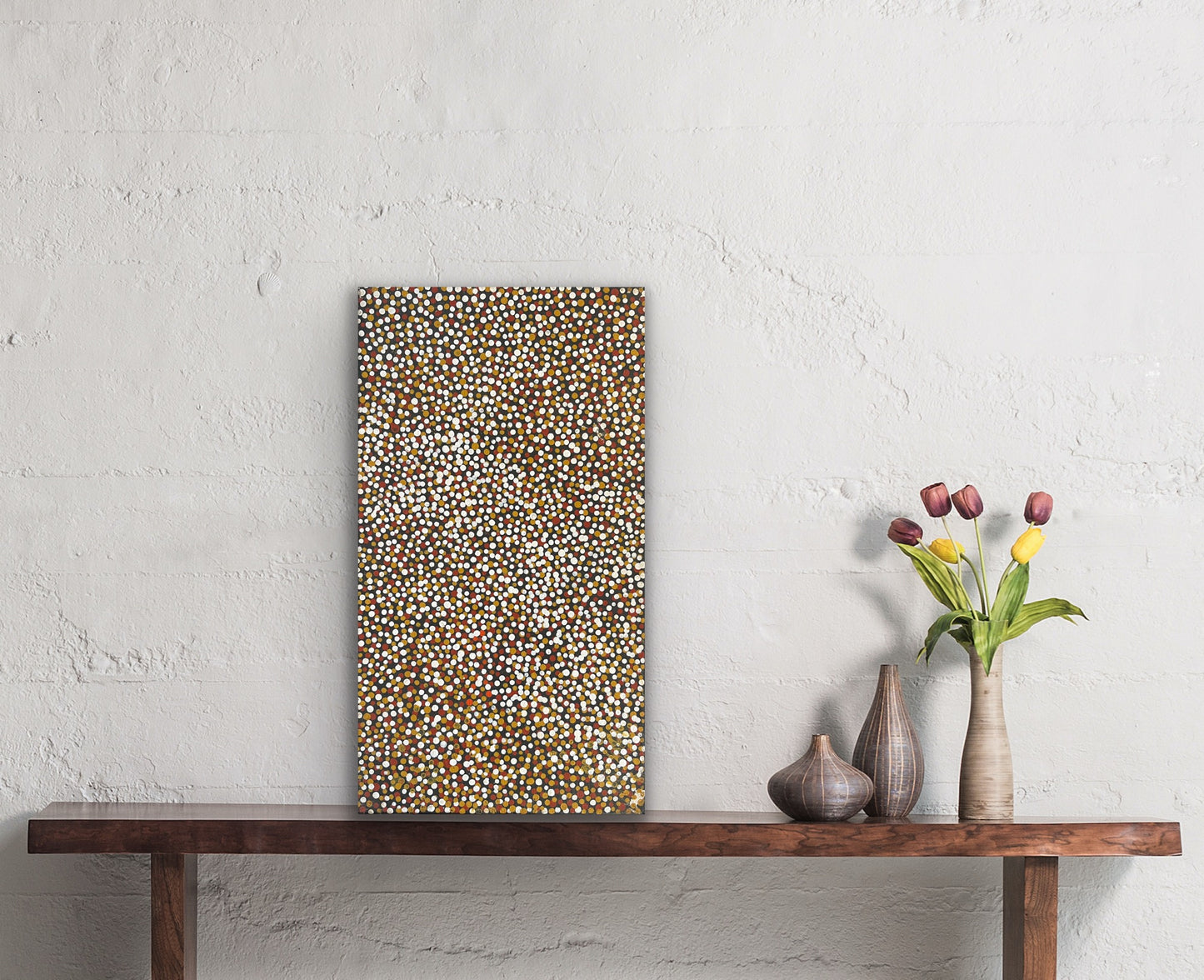 A small painting by Polly Ngale resting on a wooden console table with decorative vases and flowers.
