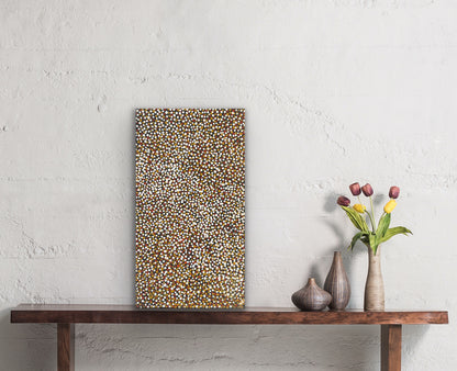 A small painting by Polly Ngale resting on a wooden console table with decorative vases and flowers.