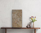 A small painting by Polly Ngale resting on a wooden console table with decorative vases and flowers.