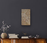 A small painting by Polly Ngale on a dark wall with a wooden cabinet below featuring books and a vase.