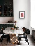 Framed Jill Daniels 'Wild Banana' artwork on a wall above dining area with a marble table and black chairs in a modern kitchen.