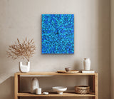 A blue painting by Selina Numina hanging on a wall above a wooden console table with decorative items.