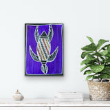 Artwork by Christine Burarrwanga depicting a sea turtle with traditional rarrk patterns on a purple background., placed on a white surface with a plant and decorative items.
