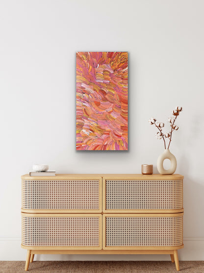A pencil yam painting by Jedda Purvis Kngwarreye featuring swirling patterns in pink, red, yellow and orange hues.