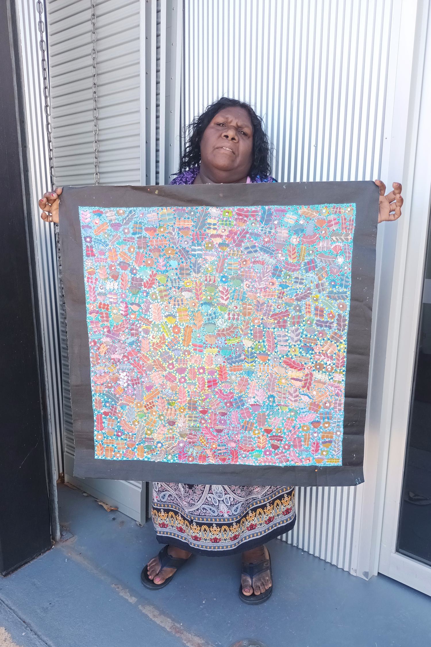 Aboriginal artist Joycie Morton Petyarre holding her bush medicine painting.