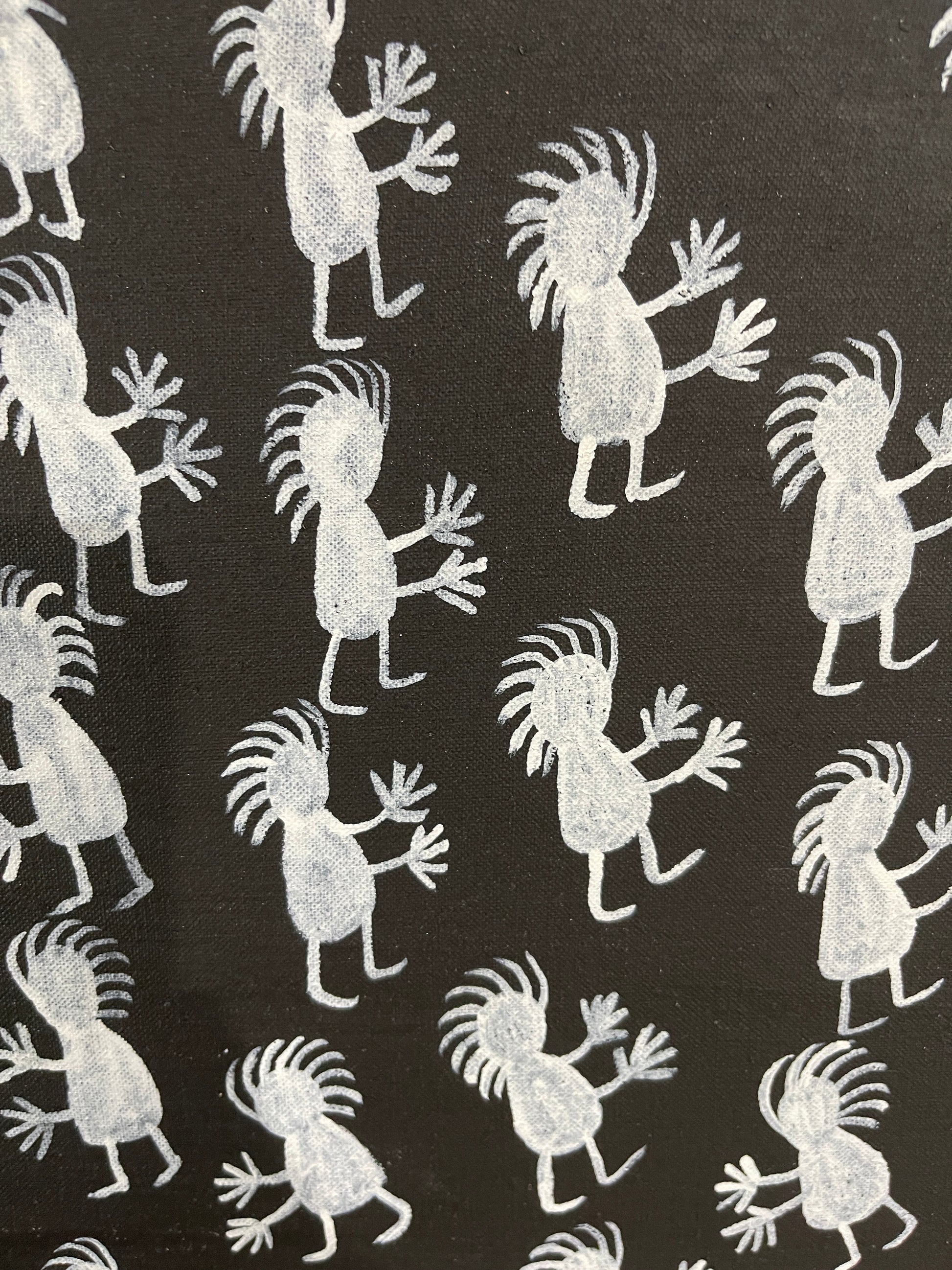 Close-up of a painting on primed linen by Naomi Kantjuriny, featuring a dark background with numerous white figures that represent good and bad spirits.