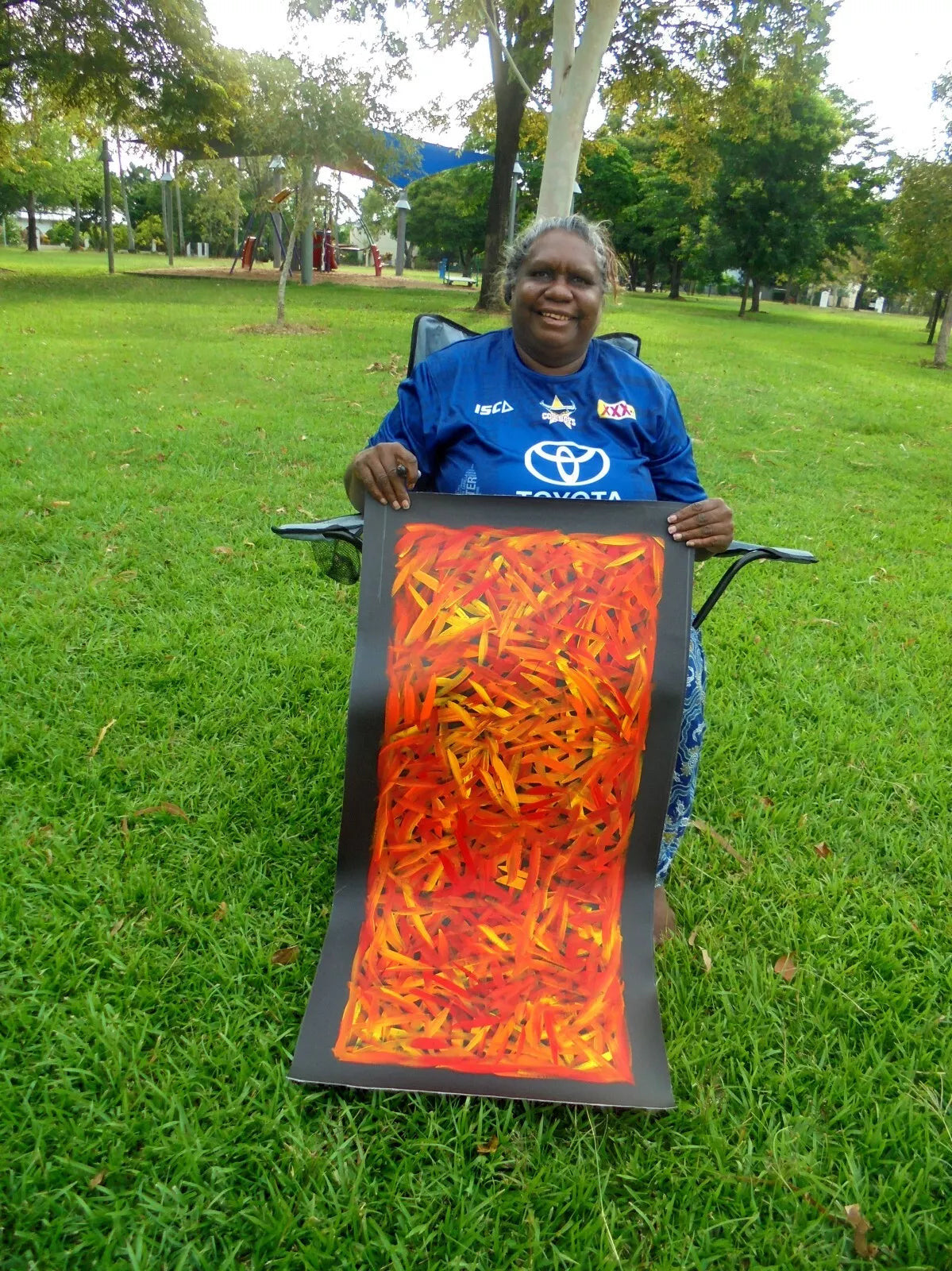 Louise Numina Napananka holding her orange and red spinifex grass paintings. 