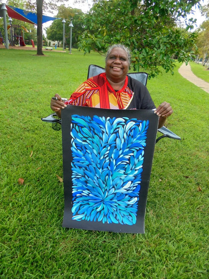 Louise Numina Napananka holding her blue bush medicine leaves paintings depicting blue and white leaves from the kurrajong bush. 