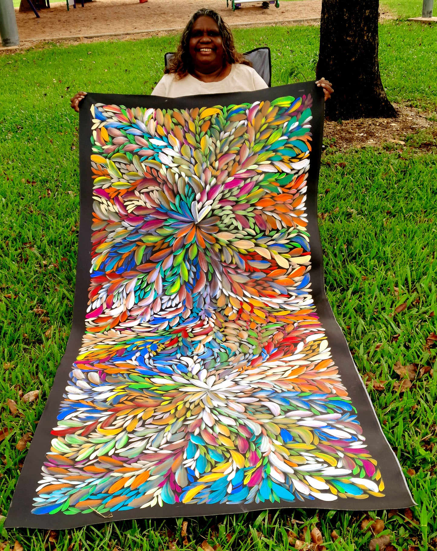 Louise Numina Napananka holding her large multicolour bush medicine leaves paintings showing leaves from the kurrajong bush which as traditionally used as bush medicine.