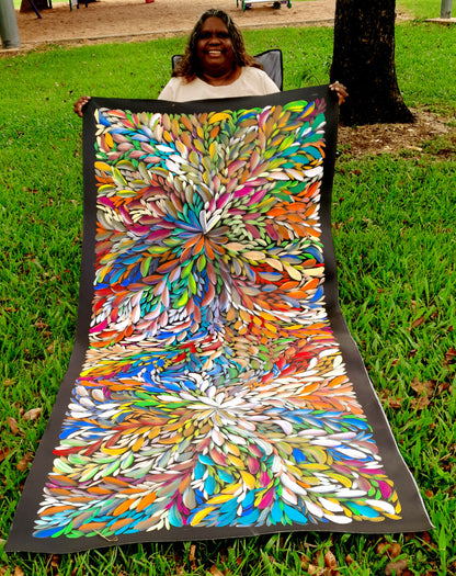 Louise Numina Napananka holding her large multicolour bush medicine leaves paintings showing leaves from the kurrajong bush which as traditionally used as bush medicine.