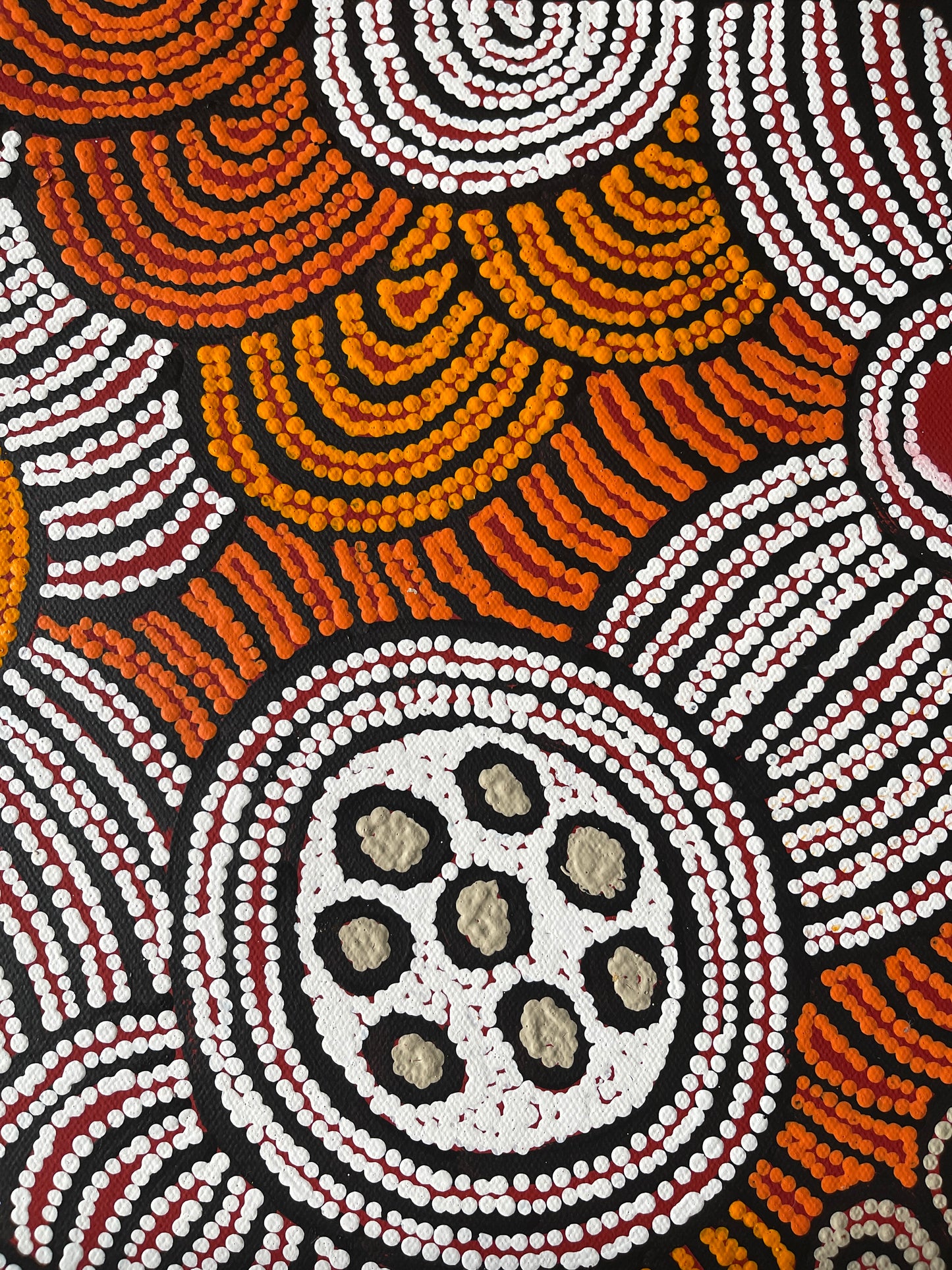 Close-up of a painting by Fiona Young Napanangka, featuring intricate dots in white, orange and red on a primed black canvas.