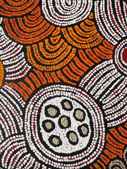 Close-up of a painting by Fiona Young Napanangka, featuring intricate dots in white, orange and red on a primed black canvas.