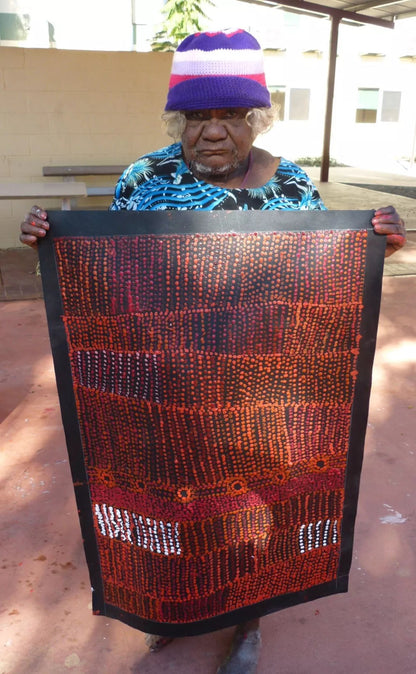 Maringka Baker holding her painting with intricate patterns in red, orange and white dots on black canvas.