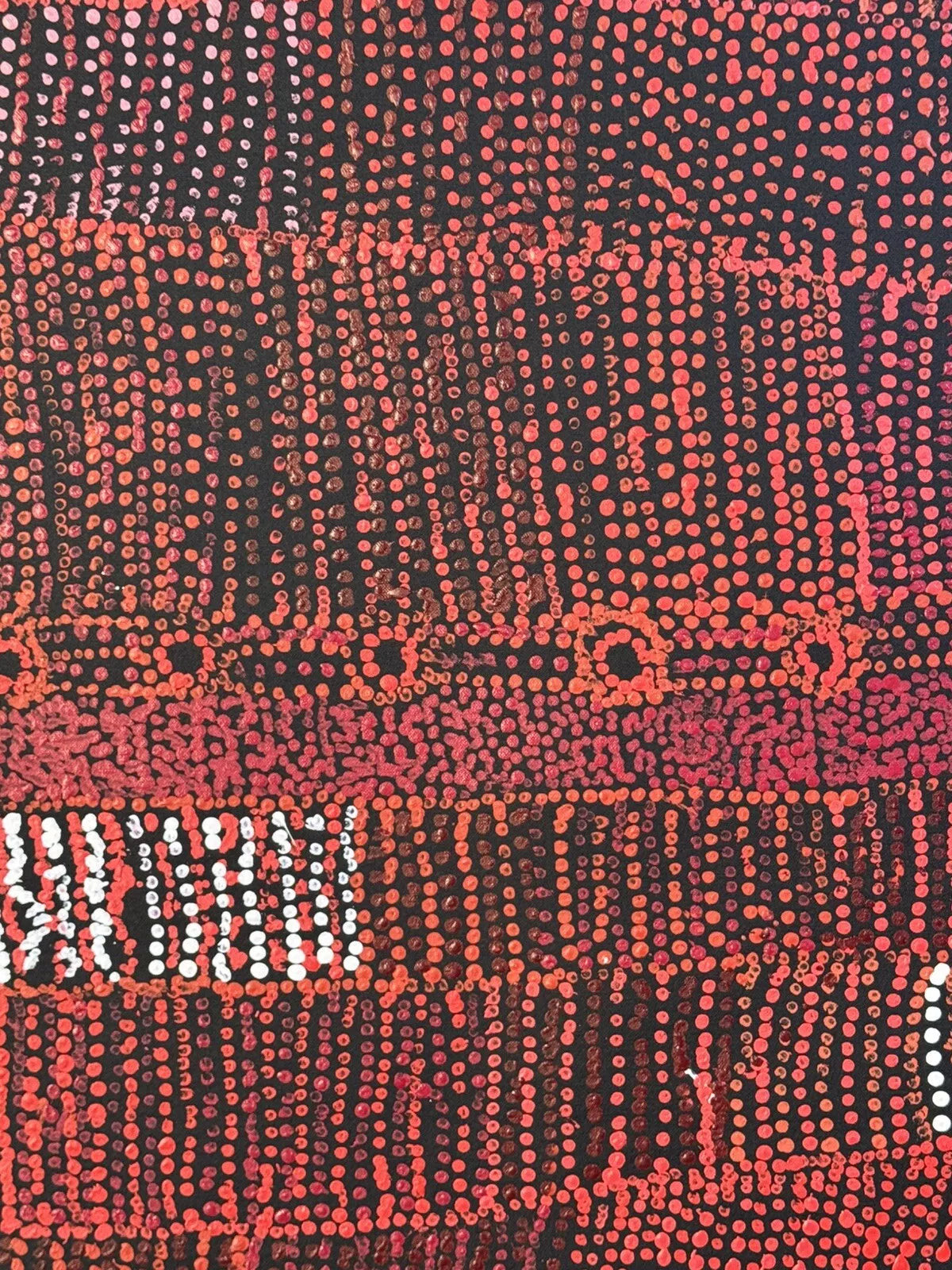 Close-up of a painting by Maringka Baker with intricate patterns in red, orange and white dots on black canvas.