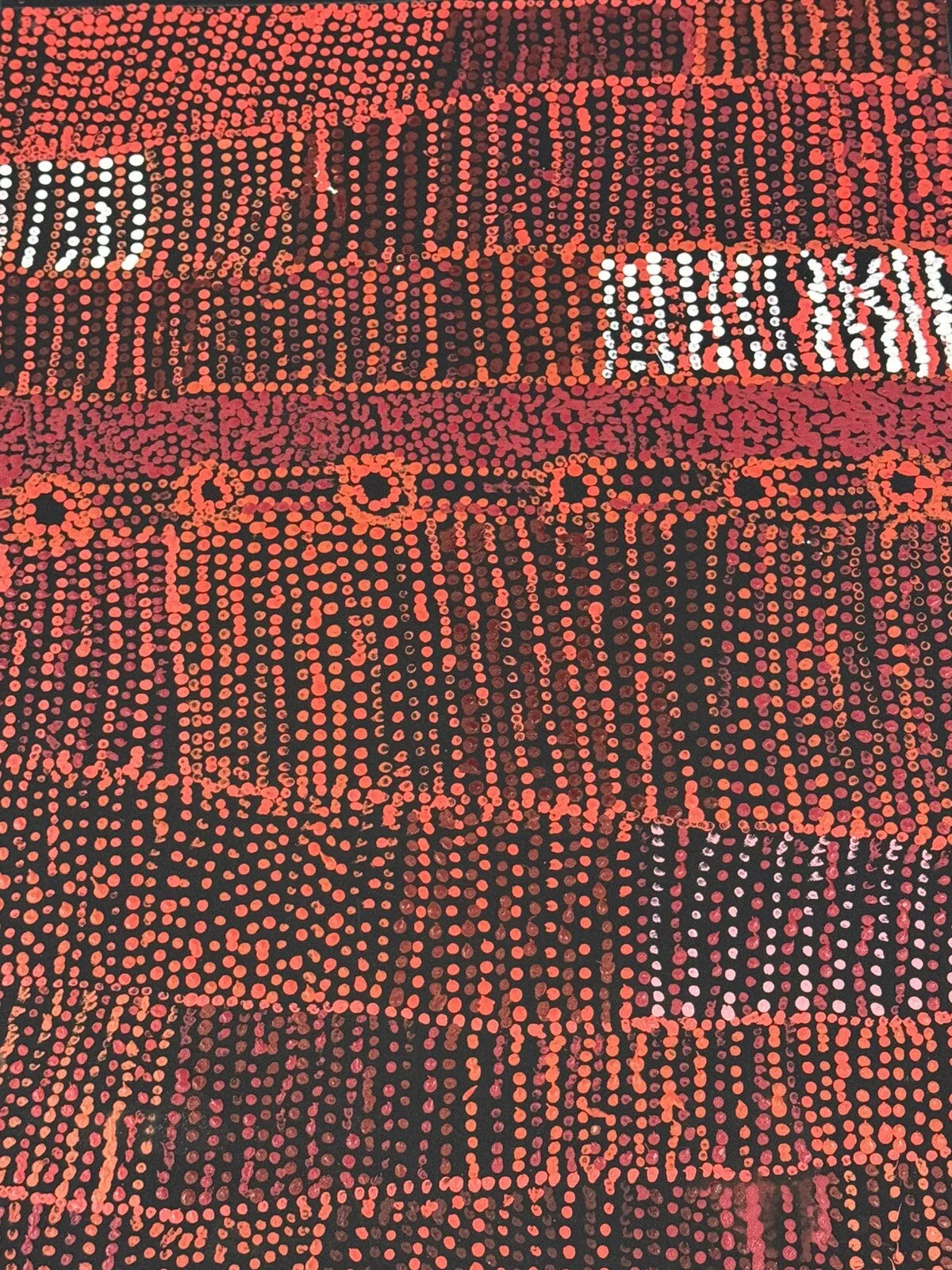 Close-up of a painting by Maringka Baker with intricate patterns in red, orange and white dots on black canvas.
