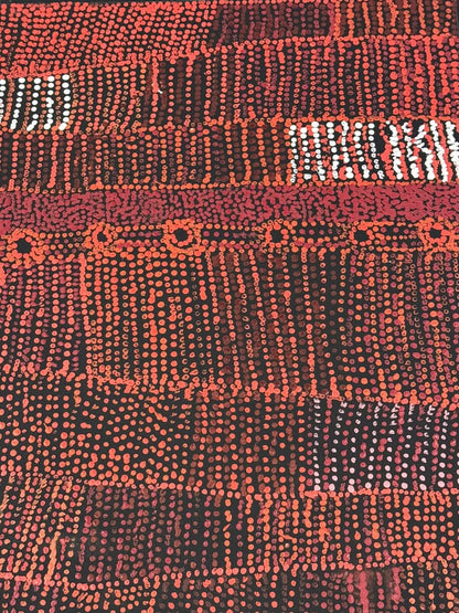 Close-up of a painting by Maringka Baker with intricate patterns in red, orange and white dots on black canvas.